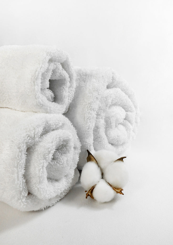 3 rolled white towels with cotton flower infant of them