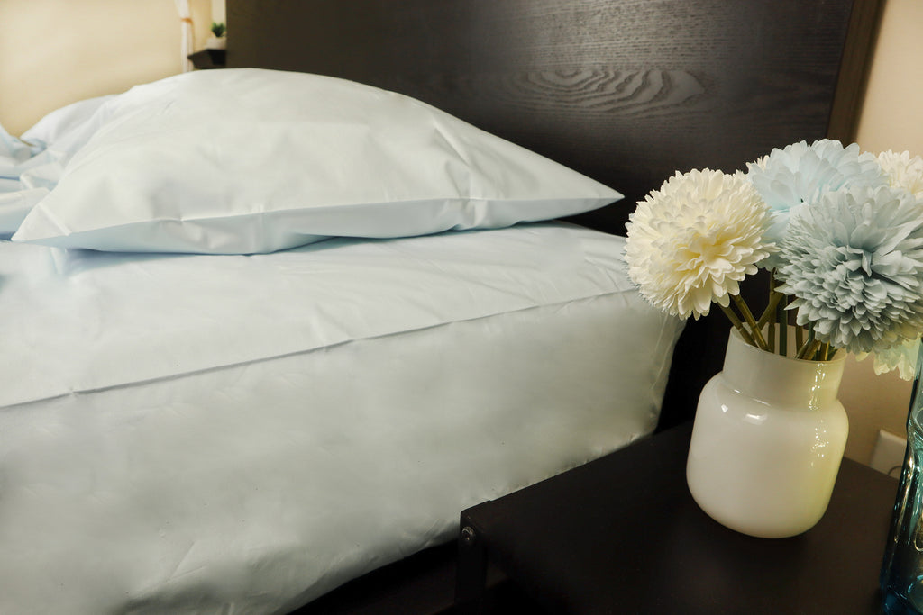 a vase with baby blue and white flowers on a night stand , bed with powder blue sheet set