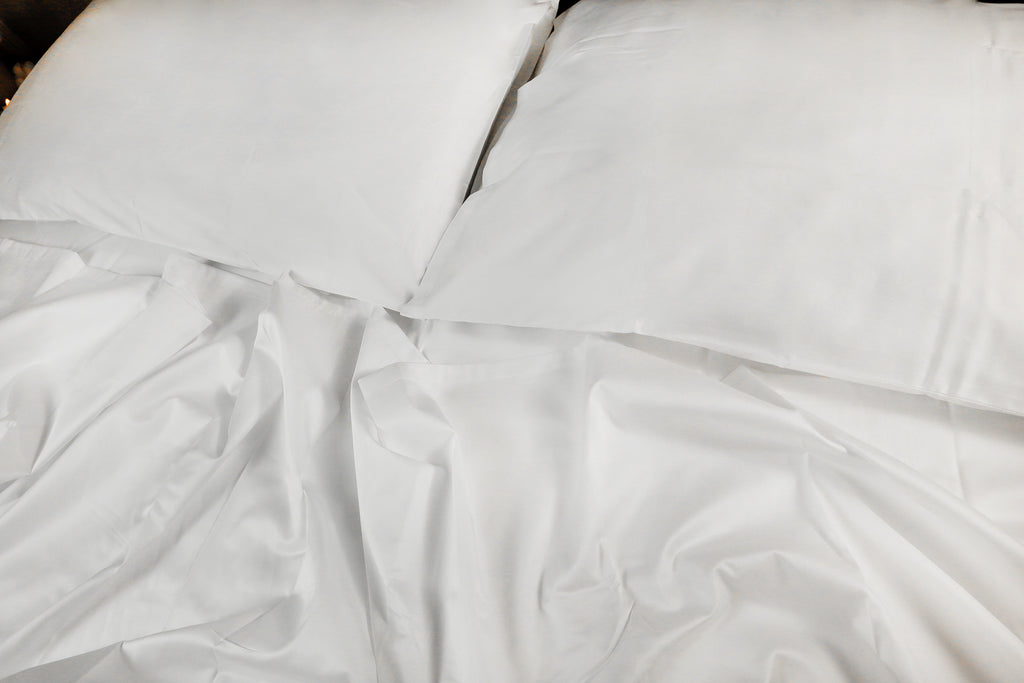 close photo of two pillow on a messy bed , pearl white sheet set