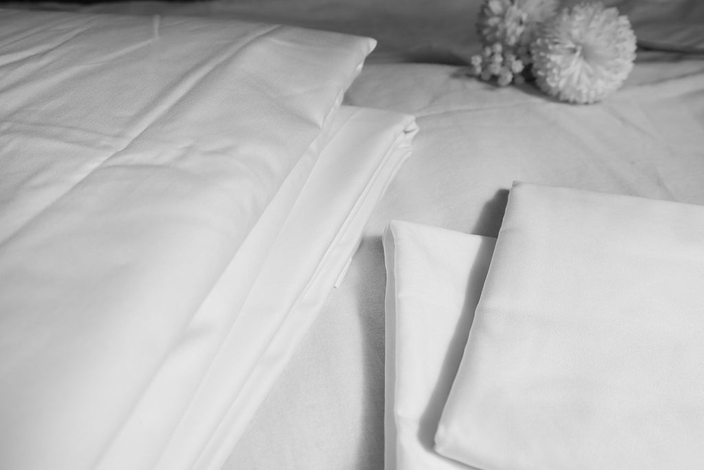 folded pearl white sheet set on a white bed + two white flowers